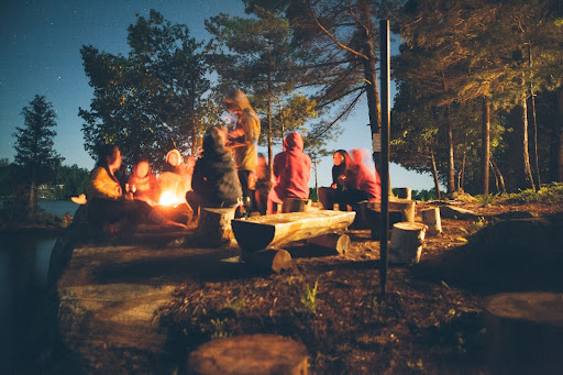 People Sitting Around Campfire At Summer Camp